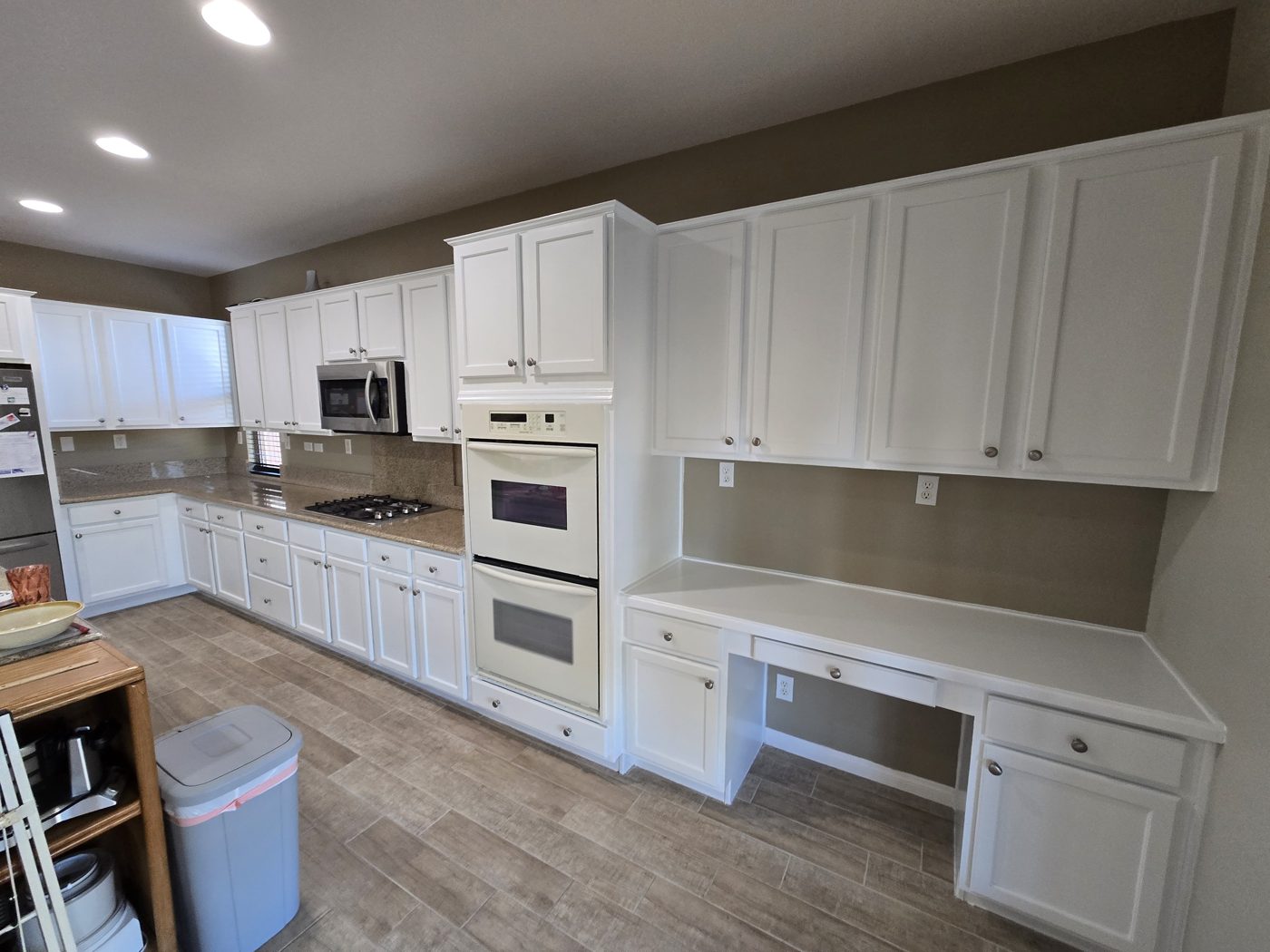 Full kitchen cabinet repaint in crisp white over wood-look flooring in Las Vegas